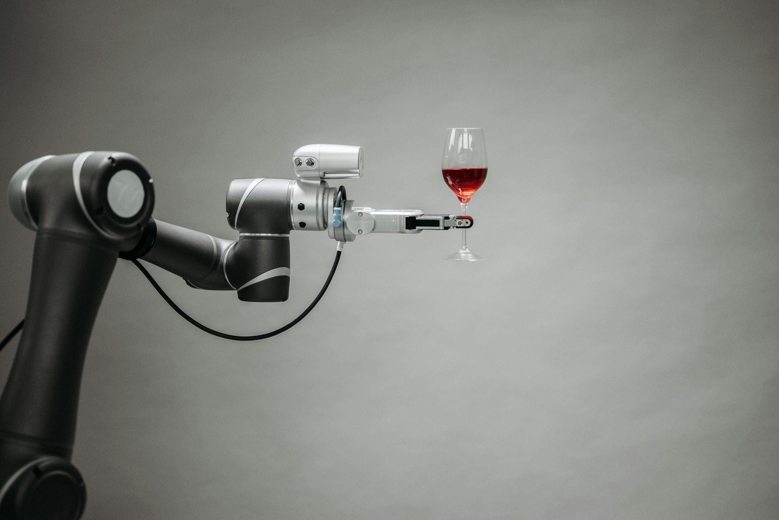 A robotic arm elegantly holds a wine glass, showcasing advanced technology in a studio setting.